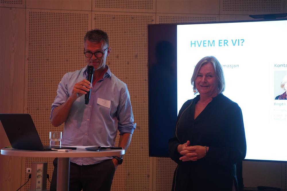 mann og dame snakker mot kamera med en skjerm bak.JPG - Klikk for stort bilde