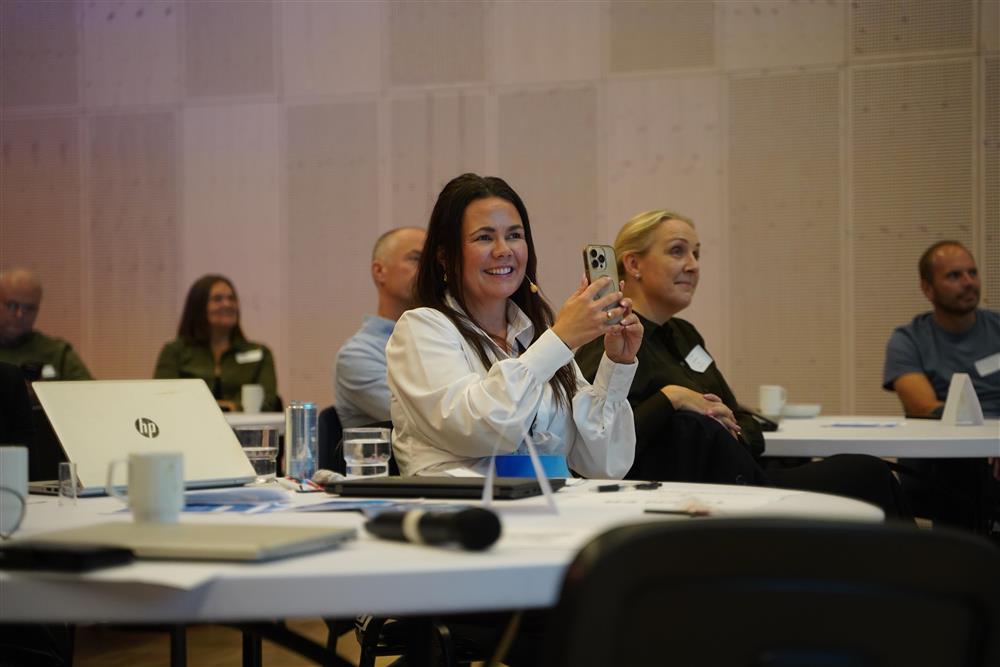 Kvinner smiler og holder opp en mobil - Klikk for stort bilde